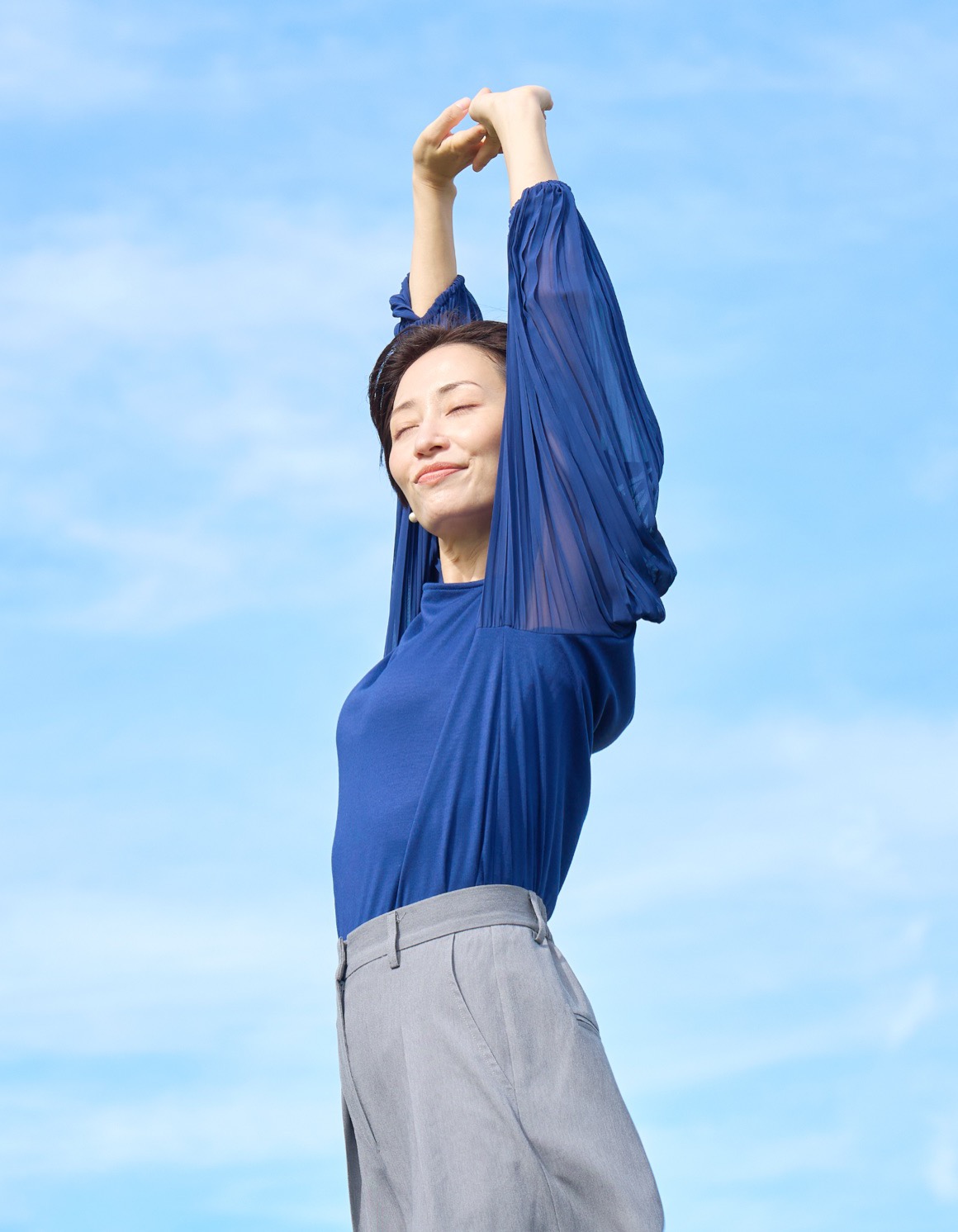青空の下で気持ちよさそうに伸びをする女性